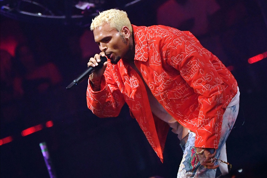 Chris Brown performs on stage in a red jacket.