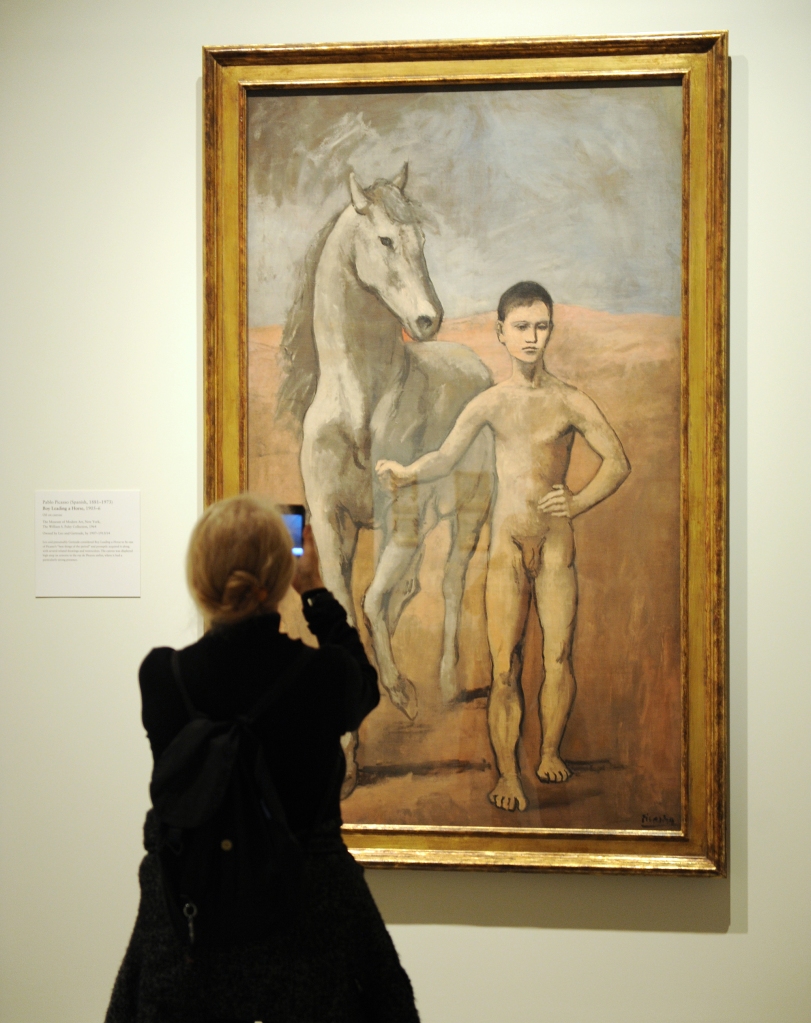 A woman takes a mobile photo of "Boy leads a horse" 1905-06 by Pablo Picasso.
